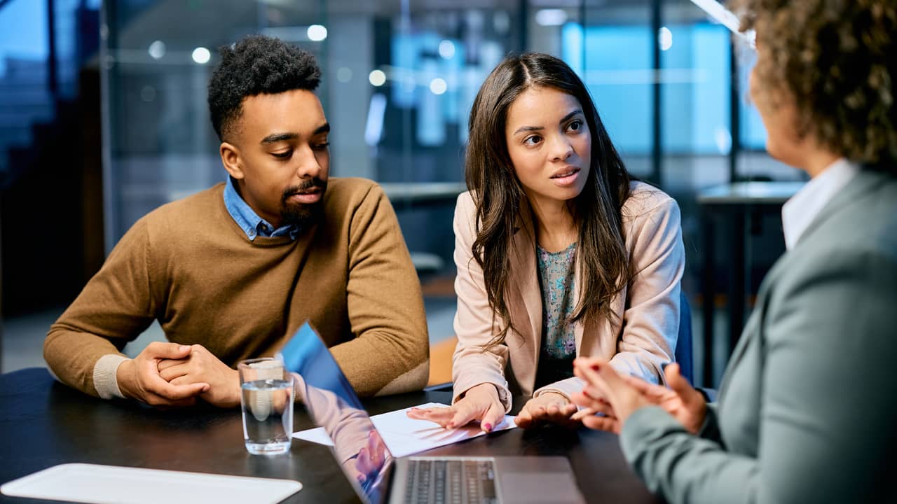 A married couple raising their insurance policy concerns to a financial advisor in an office.